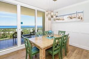 Ein Essbereich mit einem Holztisch, grünen Stühlen, Blick auf den Ozean durch eine Schiebetür und einer Pendelleuchte.
