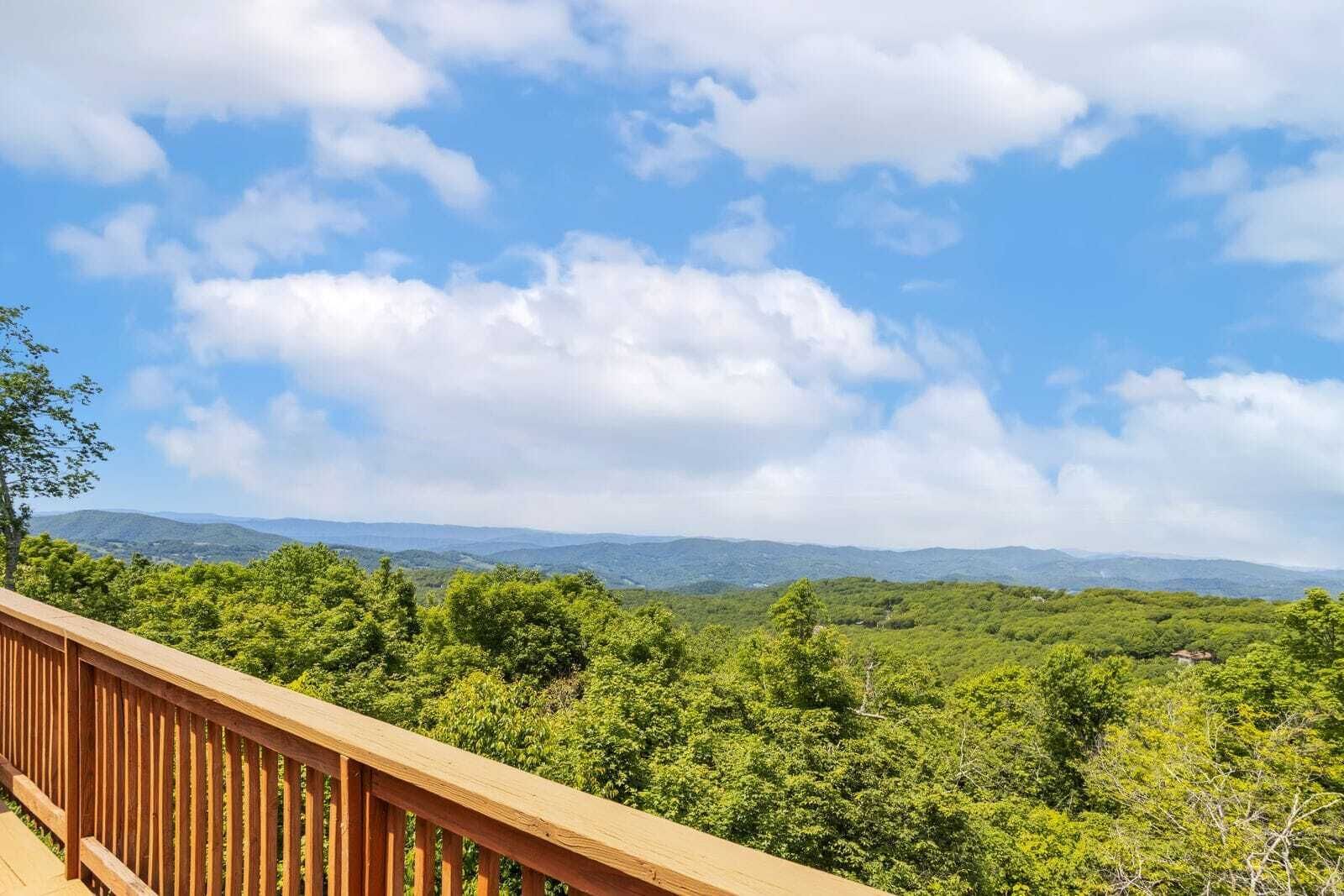 A wooden deck overlooking a forested landscape with distant mountains.