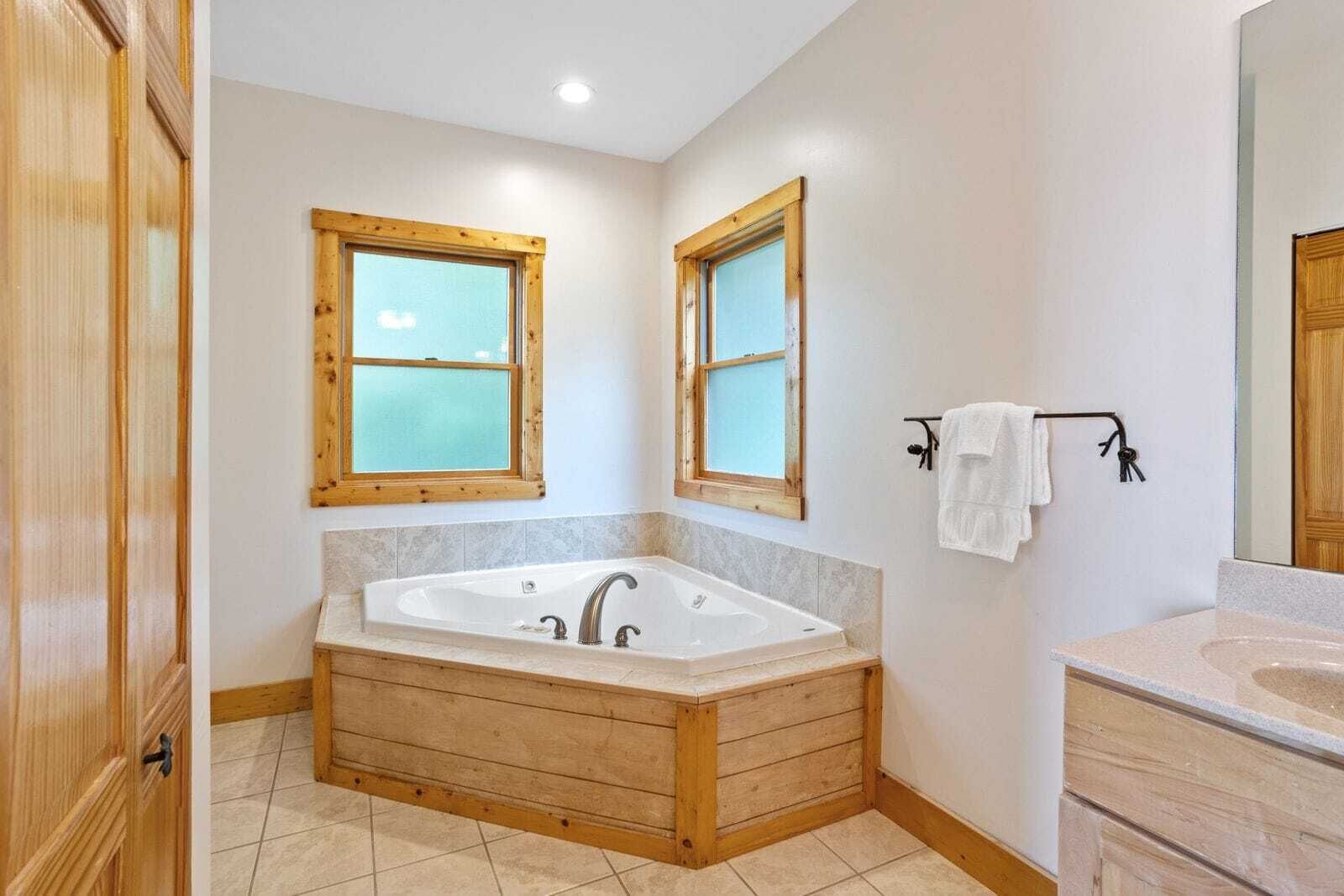 Ein Badezimmer mit einer Holzbadewanne, zwei Fenstern, einem Waschbecken und einem Spiegel.