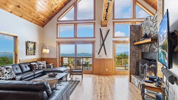 A spacious living room with a high ceiling, large windows, a fireplace, and a cozy seating area.