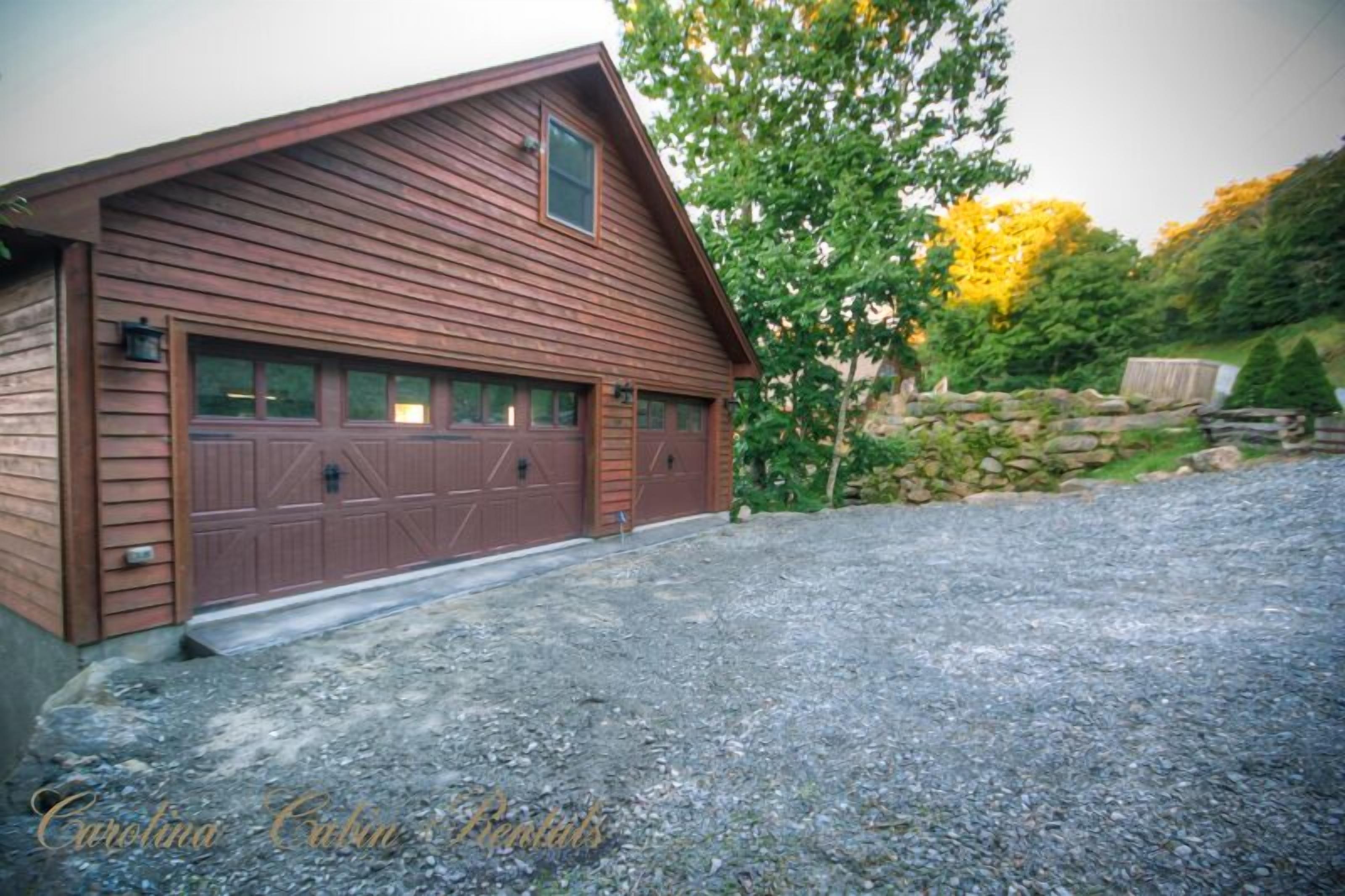 A wooden building with a garage, surrounded by a gravel driveway and greenery.
