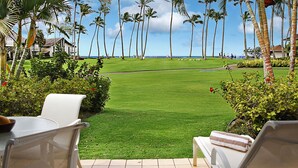 A well-maintained lawn with a few people in the distance, surrounded by palm trees and a clear sky. - Kiahuna Plantation 165 By Parrish Kauai - ocean view unit, only steps to the bea (Koloa)