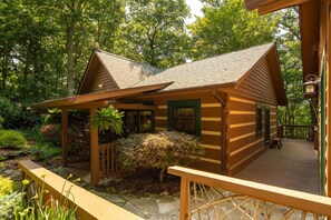 A wooden cabin with a porch, surrounded by lush greenery.