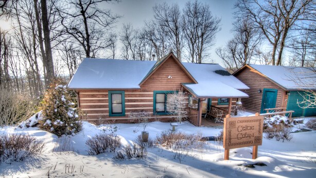 A cabin with a snow-covered roof, a porch, and a sign indicating it is a Celtic Cabin.