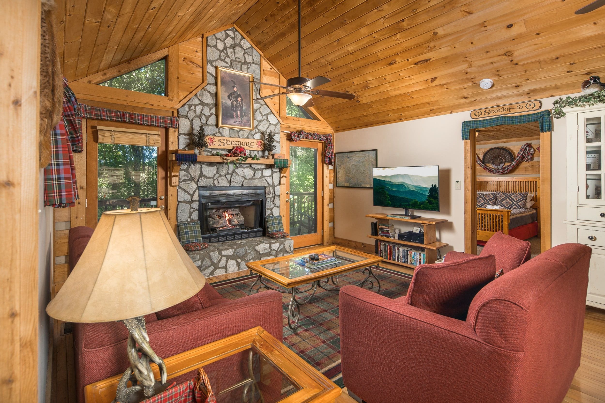 A cozy cabin interior with a stone fireplace, a television, and a plaid-covered door.