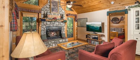 L’intérieur chaleureux d’un chalet avec une cheminée en pierre, un téléviseur et une porte recouverte d’un tissu à carreaux.