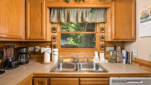A kitchen with wooden cabinets, a double sink, a coffee maker, and a window with a view of greenery.