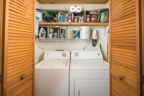 A laundry room with two front-loading washing machines, a shelf with cleaning supplies, and a hanging phone.