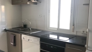 A modern kitchen with a dishwasher, oven, and double sink. There is a window with blinds and a door with a handle. - Palasiet (Villajoyosa)