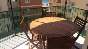 A balcony with a wooden table and chairs, overlooking a beach and other buildings. - Palasiet (Villajoyosa)