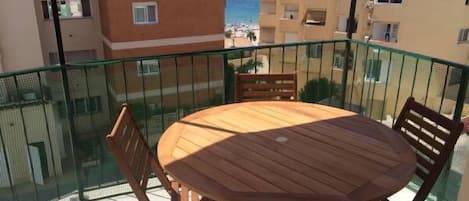 A balcony with a wooden table and chairs, overlooking a beach and other buildings.