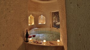 Una habitación con paredes de piedra, una bañera, velas y una botella de vino.
