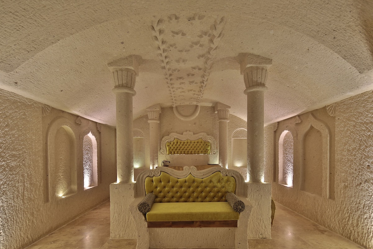 Um quarto com um sofá grande e ornamentado, colunas e teto alto com detalhes entalhados.