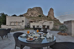 An outdoor dining area with a table set for breakfast, overlooking a mountainous landscape with ancient rock formations. - Romance Cave Suites (Nevsehir)