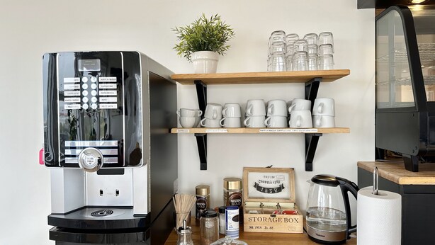Eine Kaffeemaschine, Regale mit Tassen und Bechern, eine Aufbewahrungsbox sowie ein Wasserkocher auf einem Holztisch.