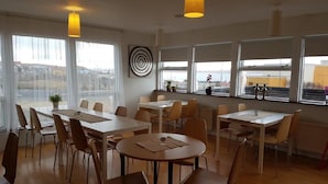 Ein moderner Essbereich mit mehreren Tischen und Stühlen, großen Fenstern mit Ausblick und Pendelleuchten.
