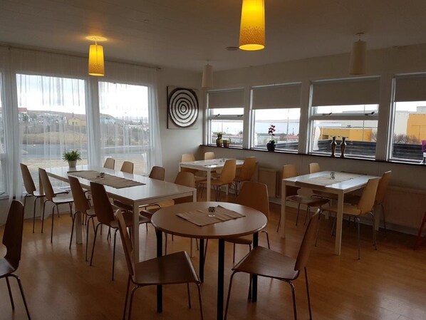 Un comedor moderno con varias mesas y sillas, ventanas amplias que ofrecen vistas, e iluminación colgante.