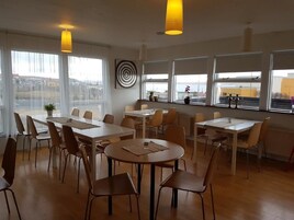 A modern dining area with multiple tables and chairs, large windows with views, and pendant lighting.