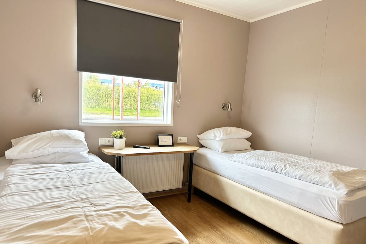 Ein Schlafzimmer mit zwei Betten, einem kleinen Tisch, einer Zimmerpflanze und einem Fenster mit Blick ins Grüne.