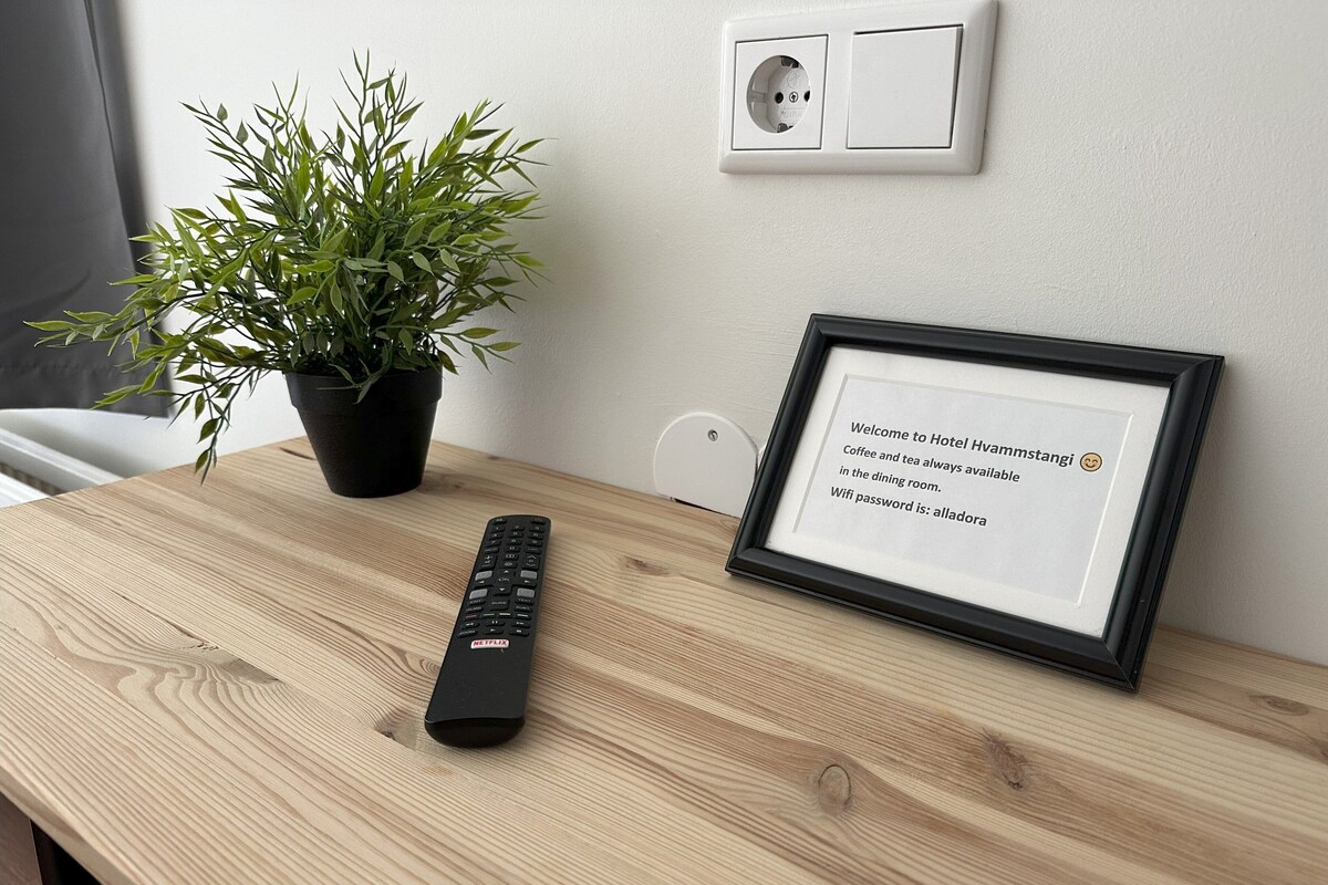 Ein Holztisch mit Fernbedienung, einem gerahmten Willkommensschild und einem Blumentopf.