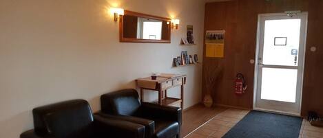 A room with a sofa, a small table, a mirror, a bulletin board, and a door with a window.