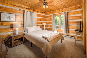A log cabin bedroom with a bed, nightstands, a ceiling fan, and a window. - Peaceful Boone Log Cabin | Mountain Views, Fireplace, Loft & Pet Friendly (Boone)