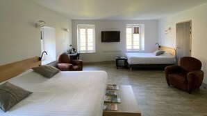 A spacious bedroom with a large bed, a smaller bed, two armchairs, a bedside table, and a TV mounted on the wall. - Lodge Hôtel Domaine De Sommedieue (Sommedieue)