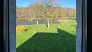 A view through a window with a metal railing, a grassy lawn, and a tree in the foreground. - Lodge Hôtel Domaine De Sommedieue (Sommedieue)