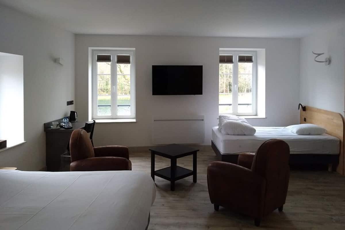 A hotel room with a bed, two armchairs, a small table, a TV mounted on the wall, and a window with a view of greenery.