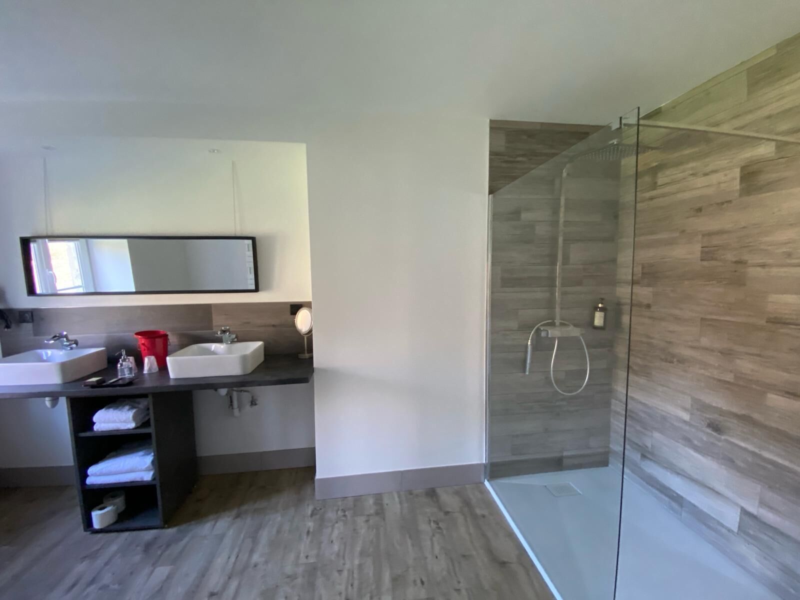 Un baño moderno con dos lavamanos, cabina de ducha de cristal y pared de madera.