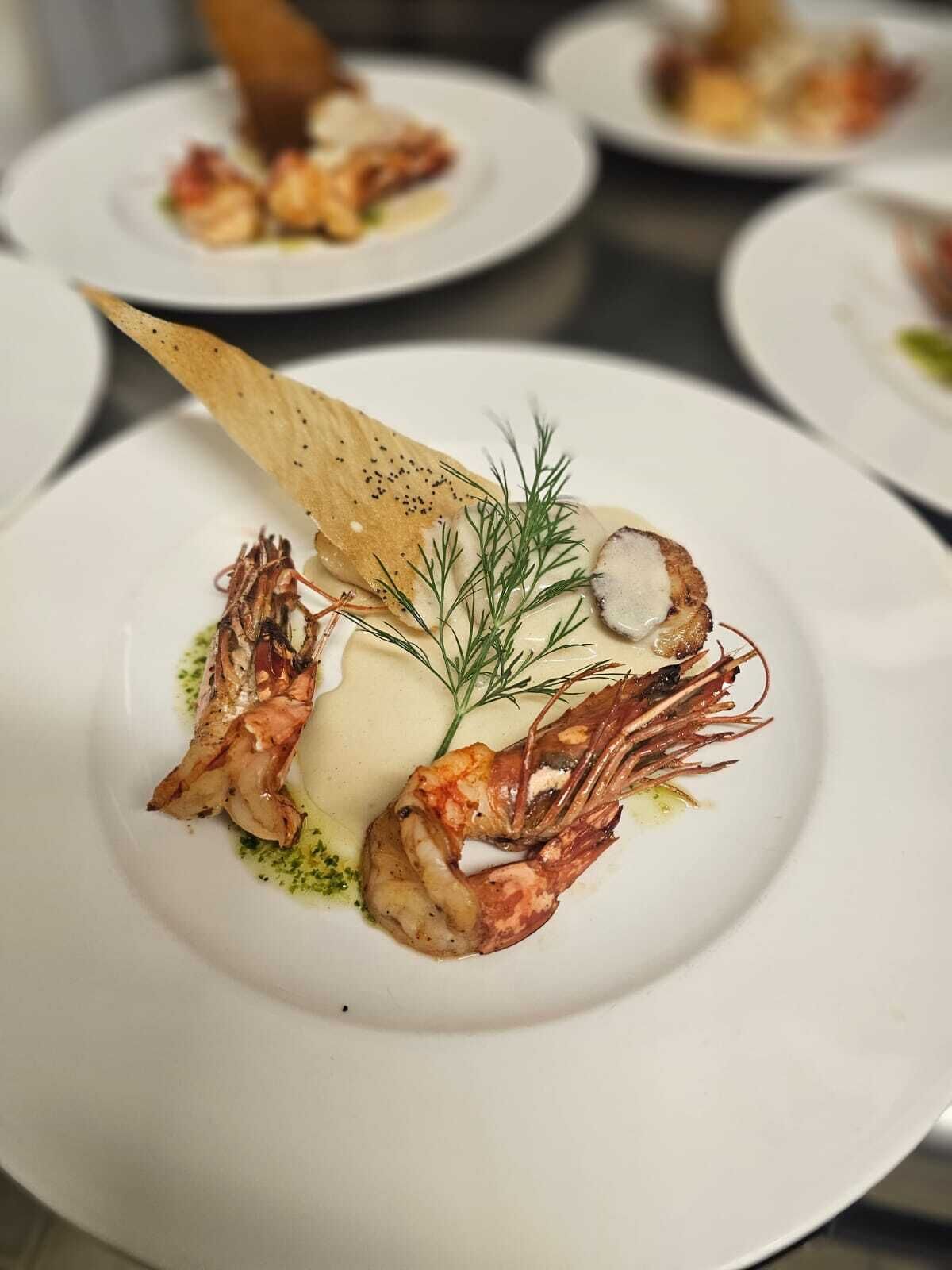 Plat amb gambes a la planxa, un tros de peix i una mica de salsa, guarnit amb julivert i una galeta.