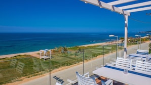 Terraza con mobiliario blanco con vista a una playa y al océano.