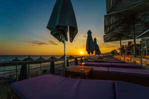 Un área de descanso en la playa con tumbonas y sombrillas, con vista al océano al atardecer.