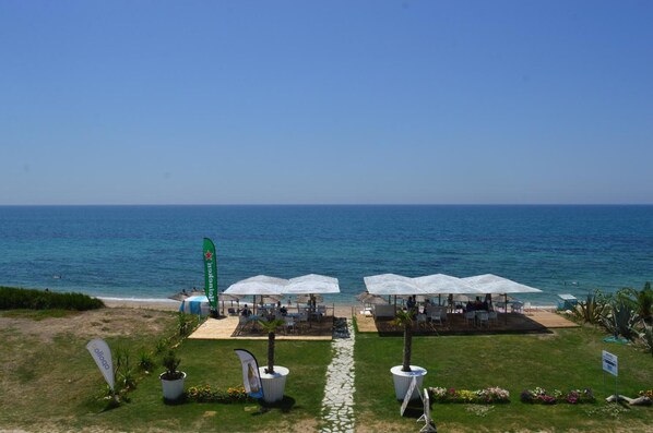 A beachside area with outdoor seating under umbrellas, a clear view of the sea, and a pathway leading to the beach. - Must Boutique Hotel (Preveza)
