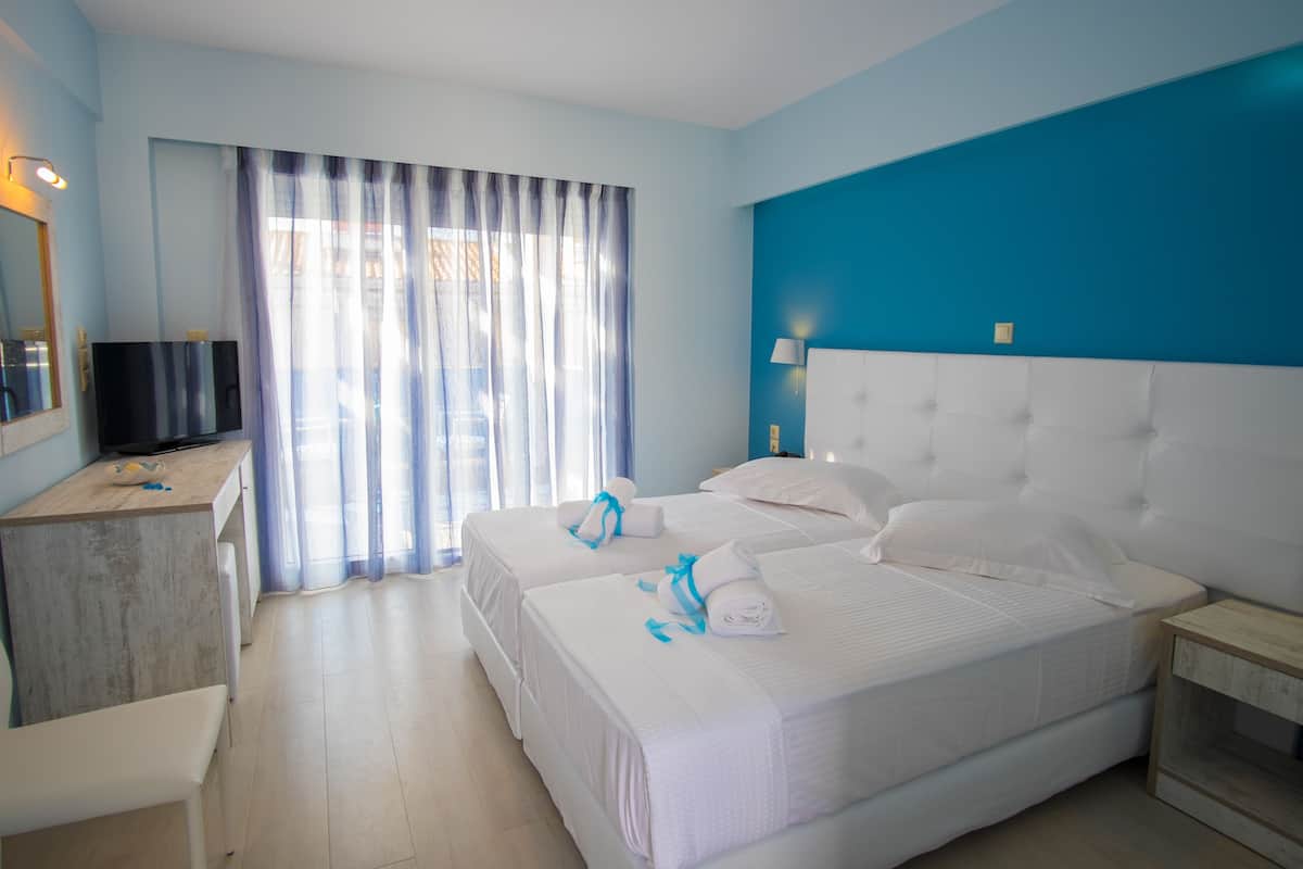 A hotel room with two beds, a desk, a television, and a window with curtains.