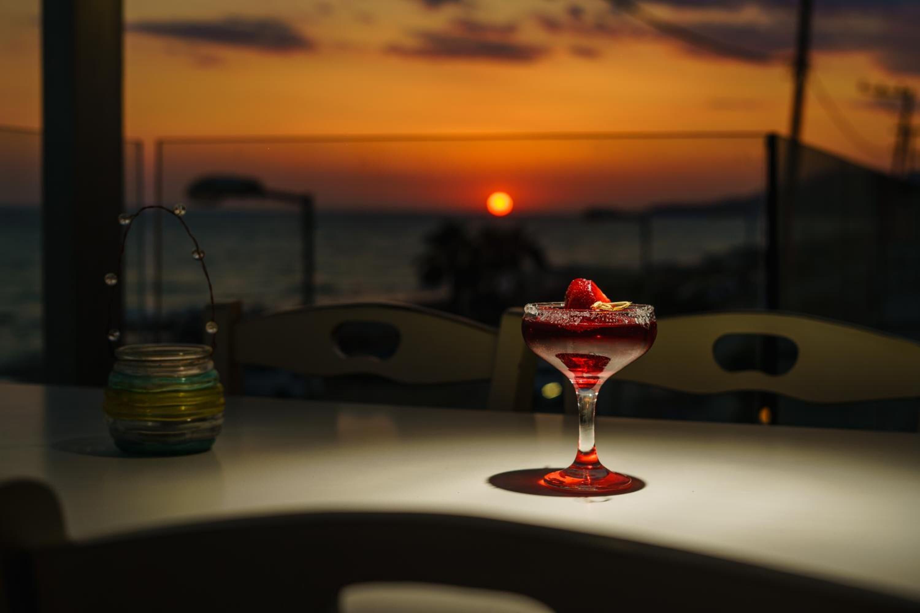 A sunset view from a balcony with a table featuring a cocktail glass and a decorative jar.