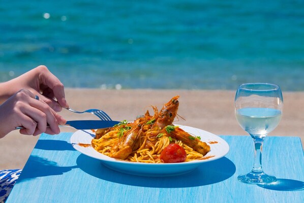 Un plato de pasta de mariscos con una copa de vino blanco sobre una mesa azul junto al mar.