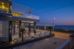Un hotel moderno con mesas al aire libre, un bar y vistas al mar.