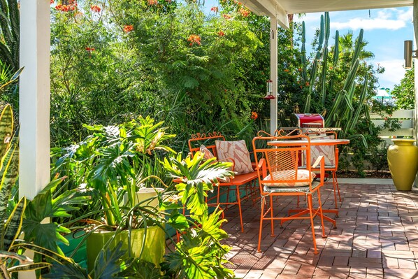 An outdoor patio with a table and chairs, surrounded by potted plants and cacti.