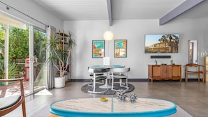 A modern living room with a round table, two chairs, a TV, and artwork on the wall.