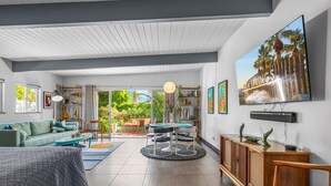 A spacious living area with a sofa, a dining table, and a TV mounted on the wall.