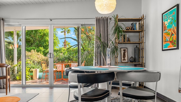 A modern dining area with a round table, black chairs, and a large window overlooking a garden.