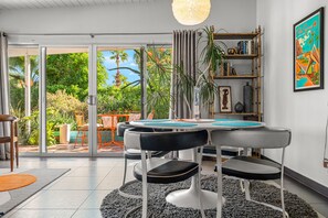 A modern dining area with a round table, black chairs, and a large window overlooking a garden.