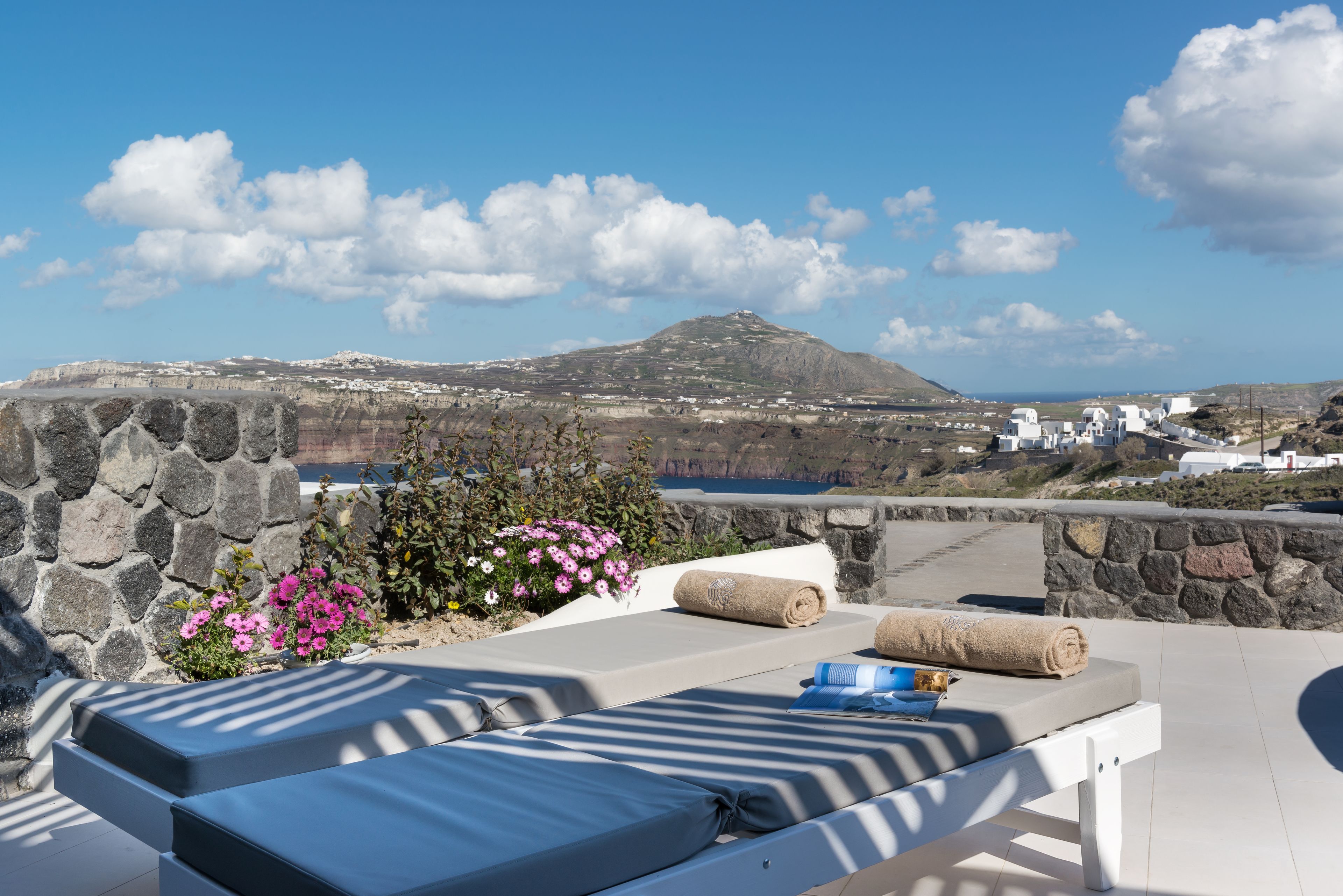 A sun lounger with a stone wall backdrop, a view of a coastal landscape, and a stone pathway.