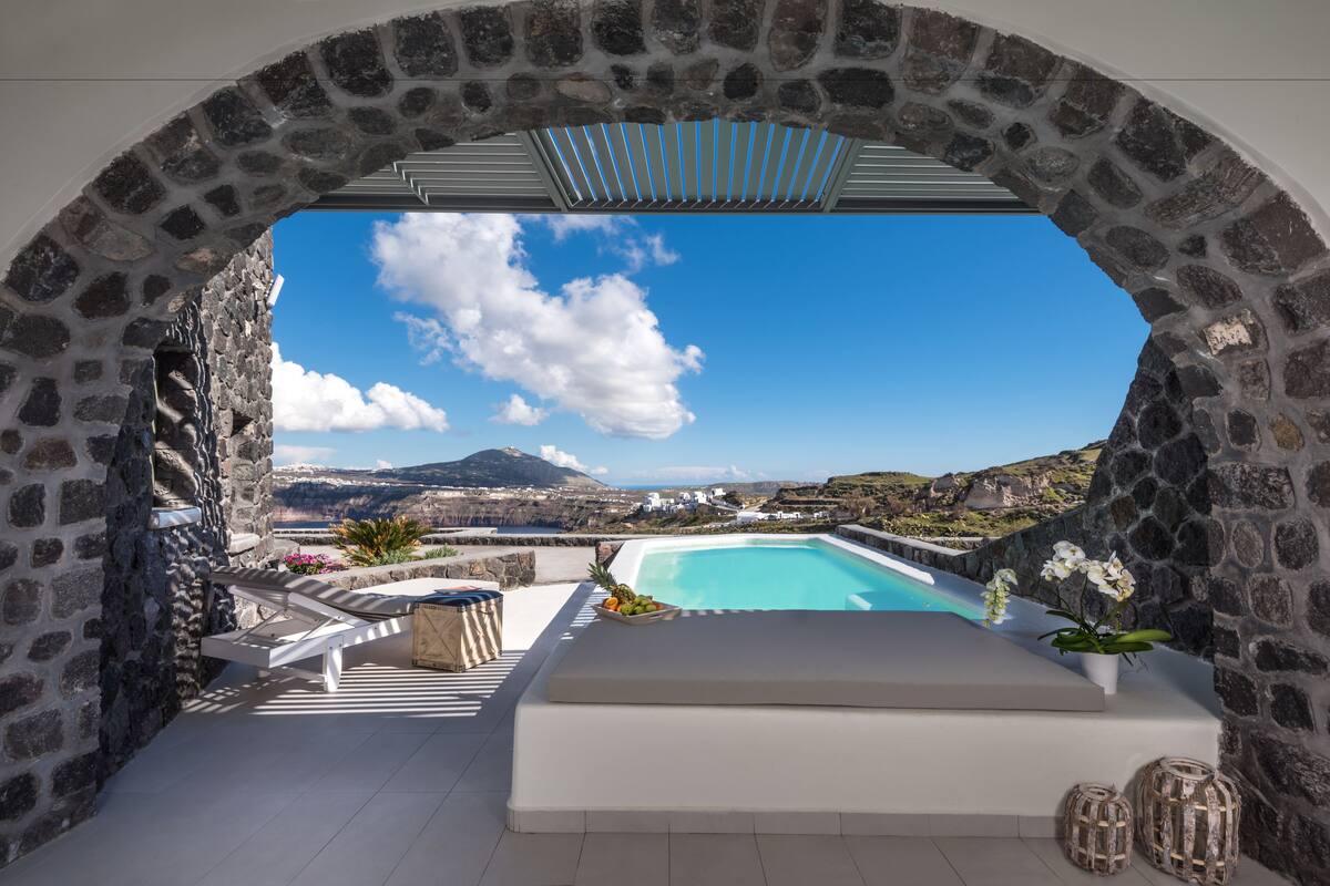 A stone archway leading to a pool area with a view of a mountainous landscape.