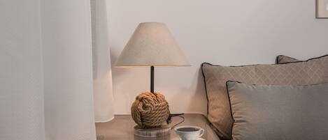 A modern room with a round, rope-wrapped lamp on a wooden coaster, a white cup on a saucer, and a sofa with patterned cushions.
