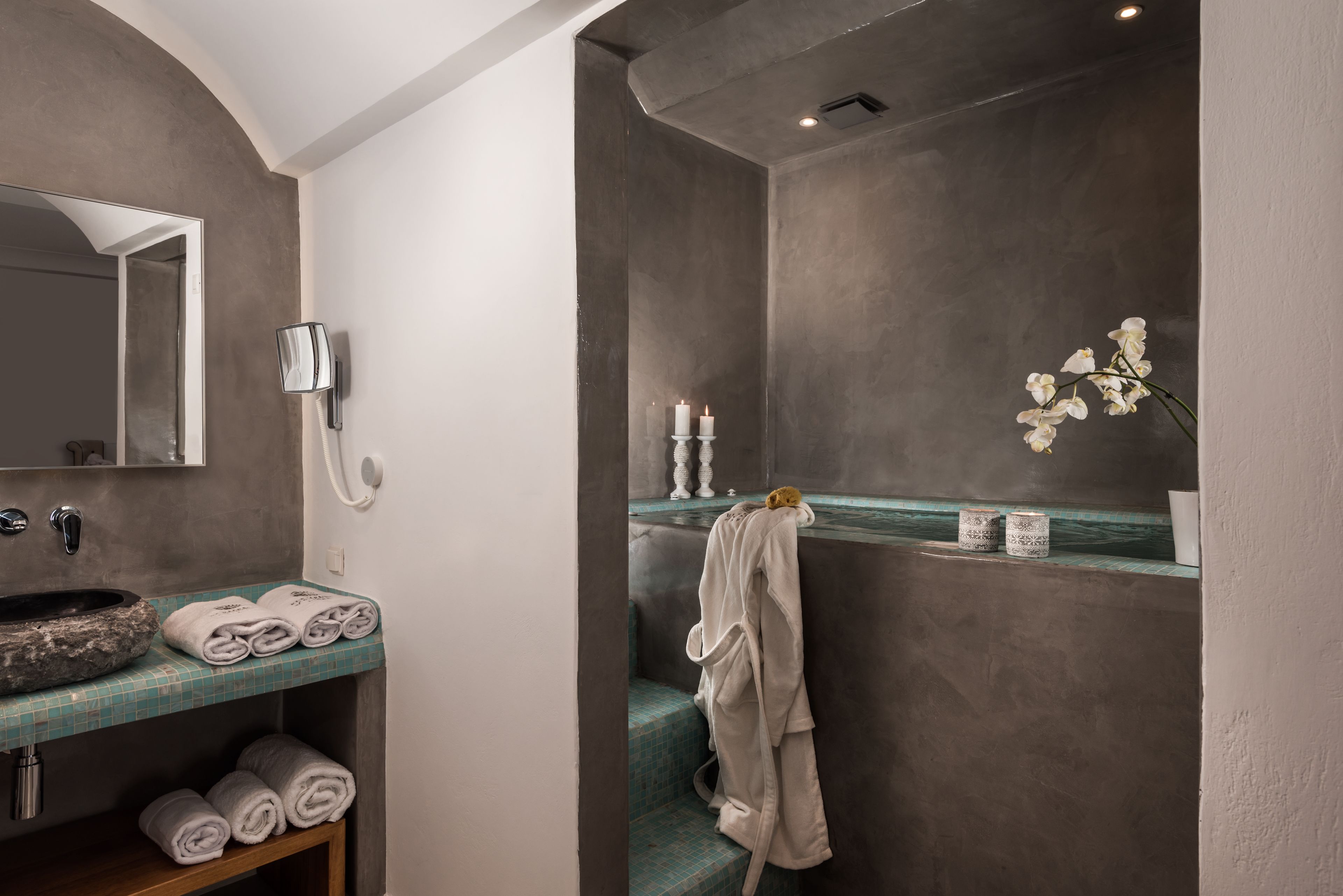 A bathroom with a stone sink, towels, a robe, a mirror, a phone, and a vase with flowers.