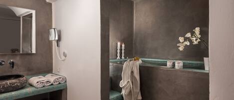 A bathroom with a stone sink, towels, a robe, a mirror, a phone, and a vase with flowers.