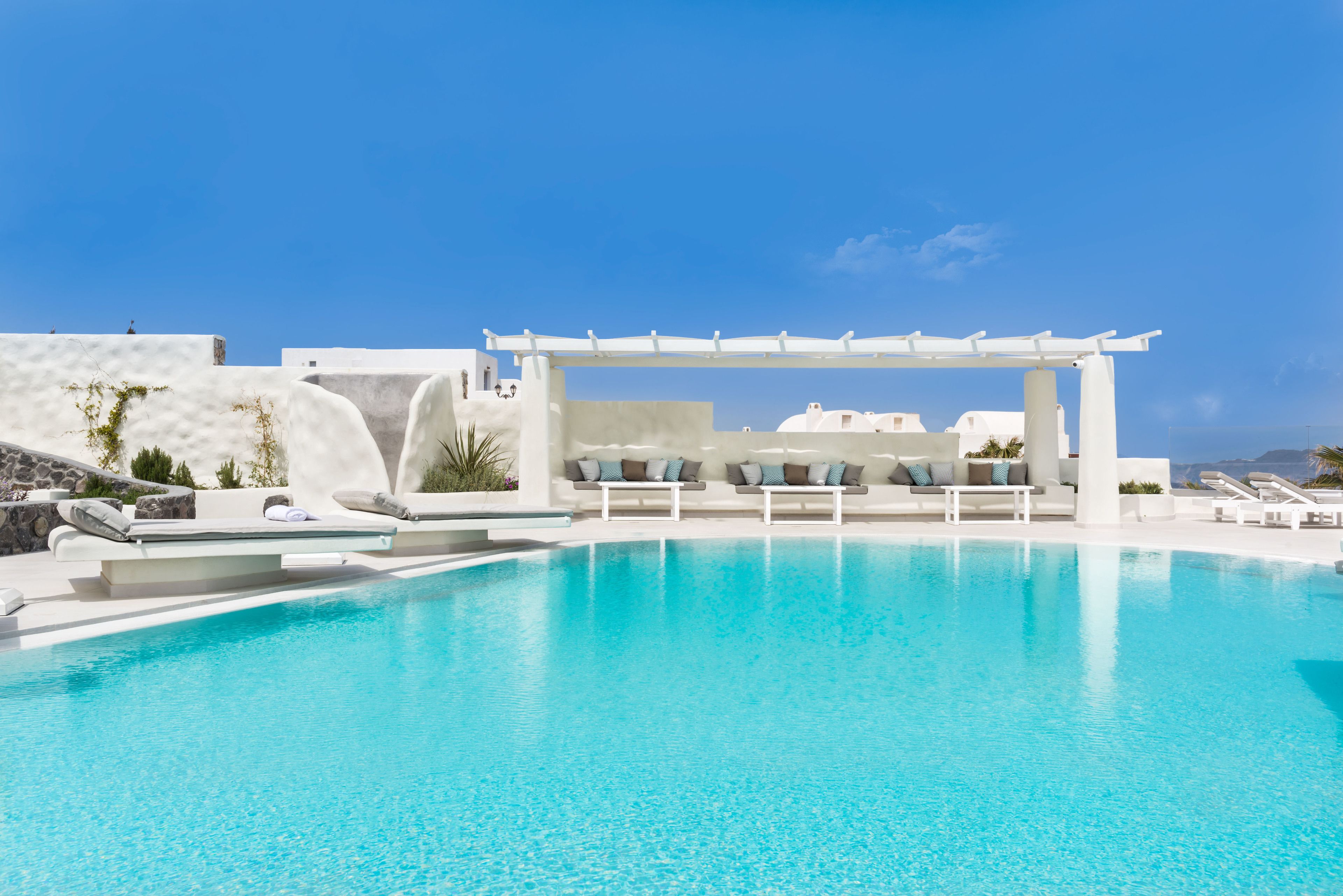 A clear blue pool with white lounge chairs and a pergola.