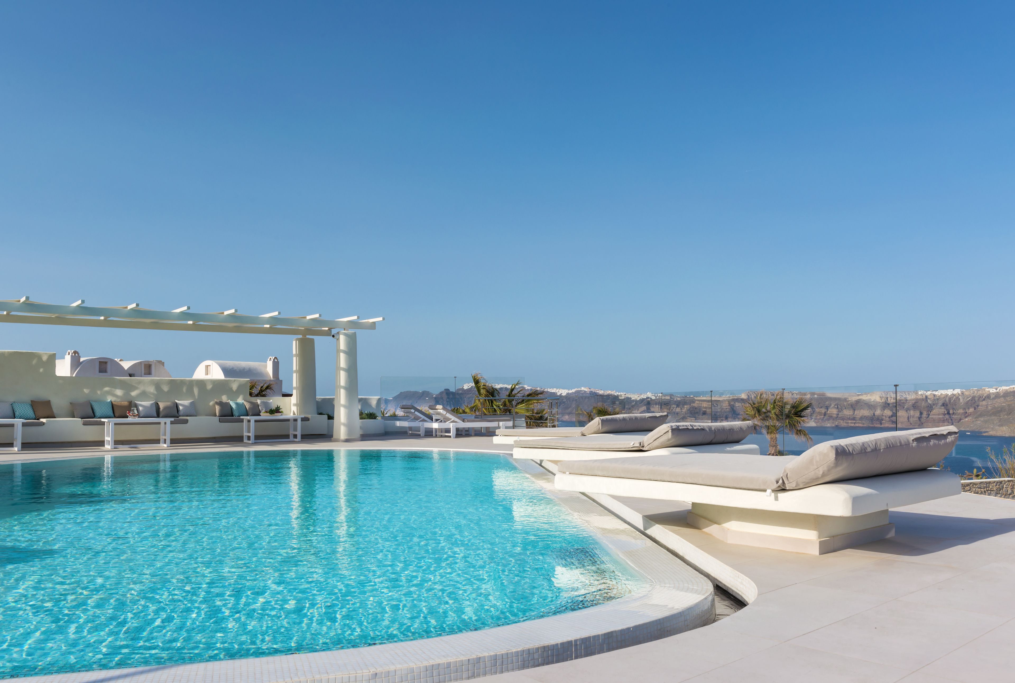 A pool area with lounge chairs and a pergola, overlooking a scenic landscape.